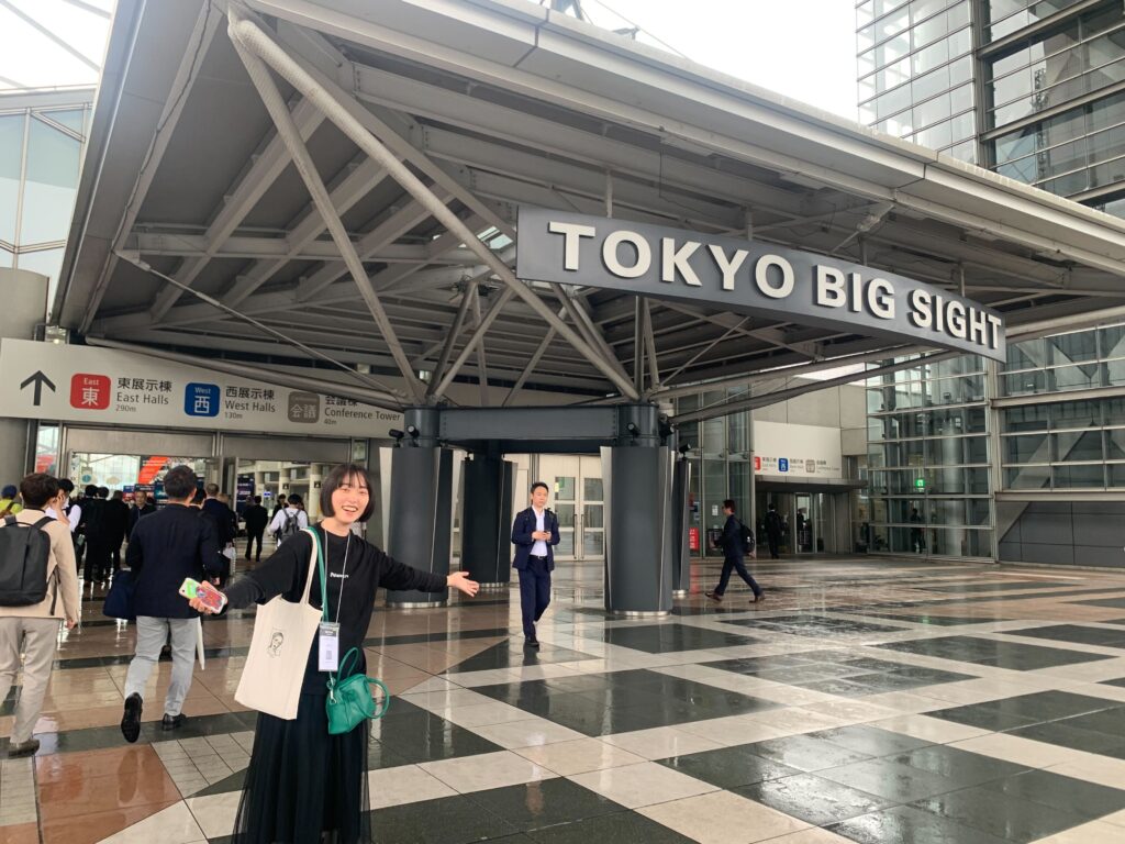 東京ビッグサイトの入り口前で、手を広げて立つノベルティ女性社員。