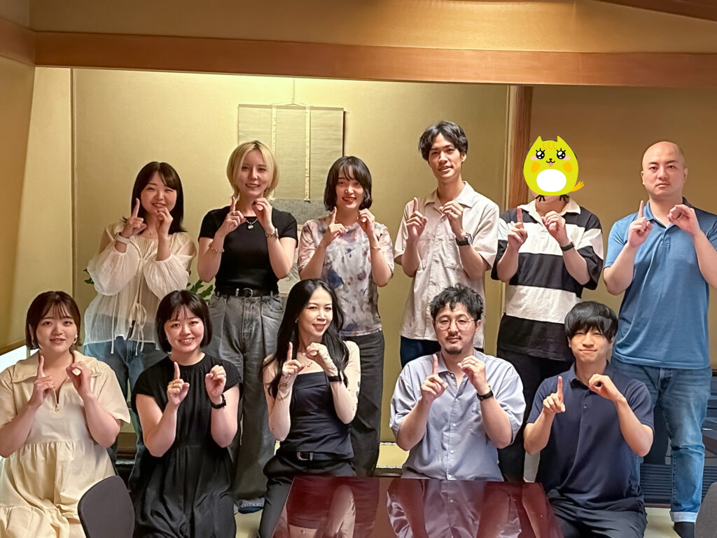 船橋市のうなぎ屋「稲荷屋」にて、指で10のポーズをとっているノベルティ社員の集合写真。