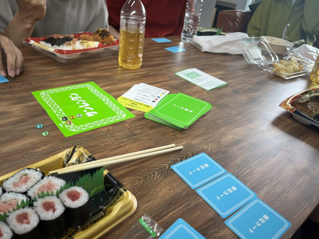 昼食をとりながらボードゲームを行うノベルティ社員。